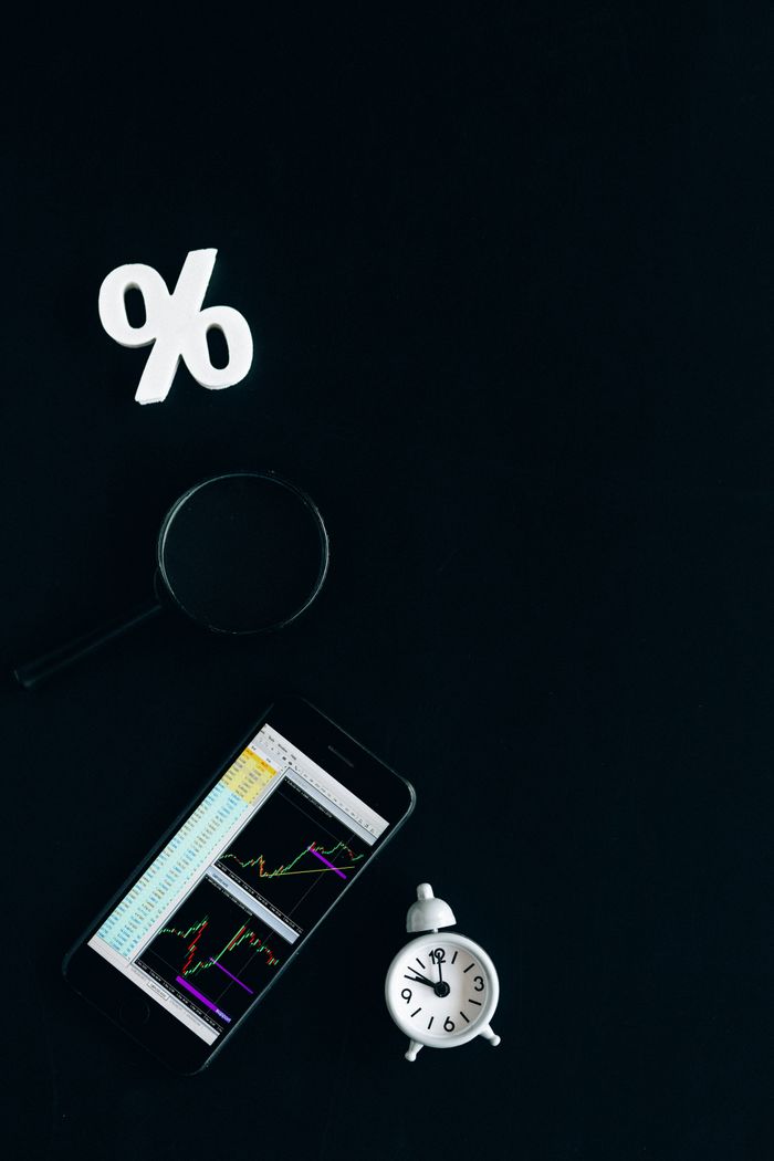 About Smartphone displaying stock market charts with a magnifying glass and clock on a black background.